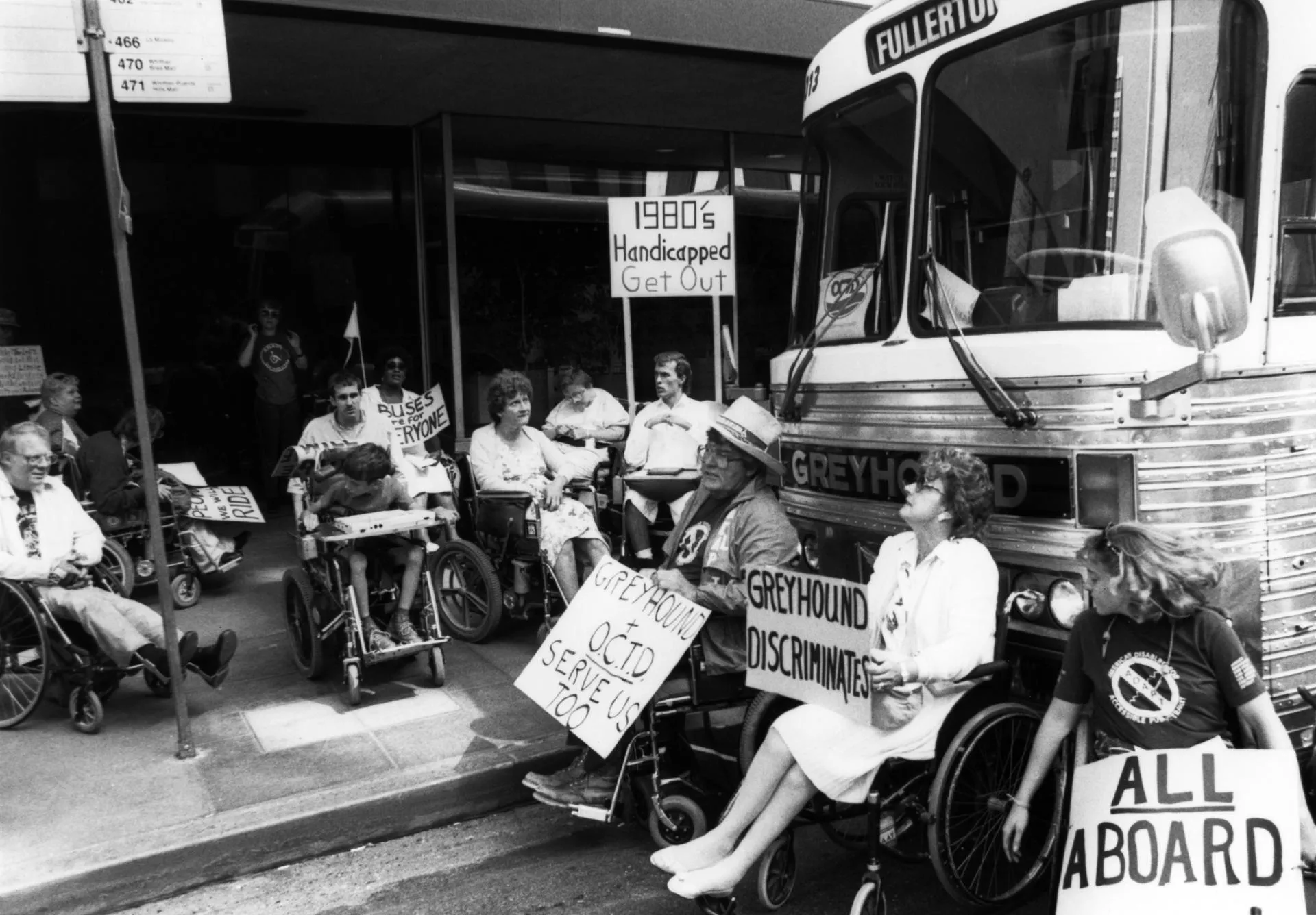 Greyhound bus depot in LA, Bill Zuke, Bill Bolte, Yvonne Nau, Sylvia Drzeweicki, Susan Gross, Ed Tessier, Ryan Duncanwood protestors with protest signs gathered on the sidewalk and front of a parked bus in the street.
