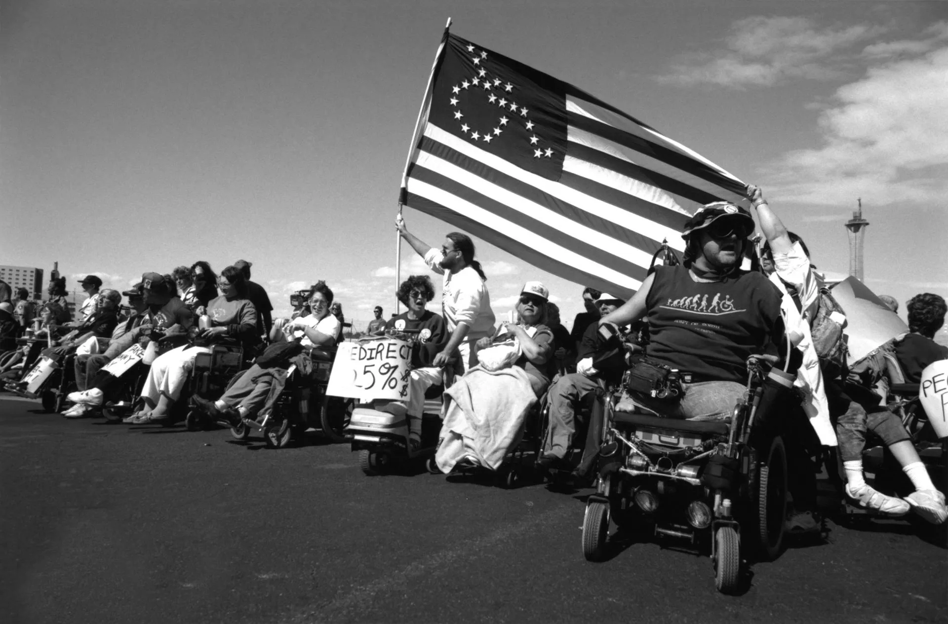 	March in Los Vegas, with an American flag in which the stars make up a figure in a wheelchair, and a large wooden cross from which an empty wheelchair hangs.
