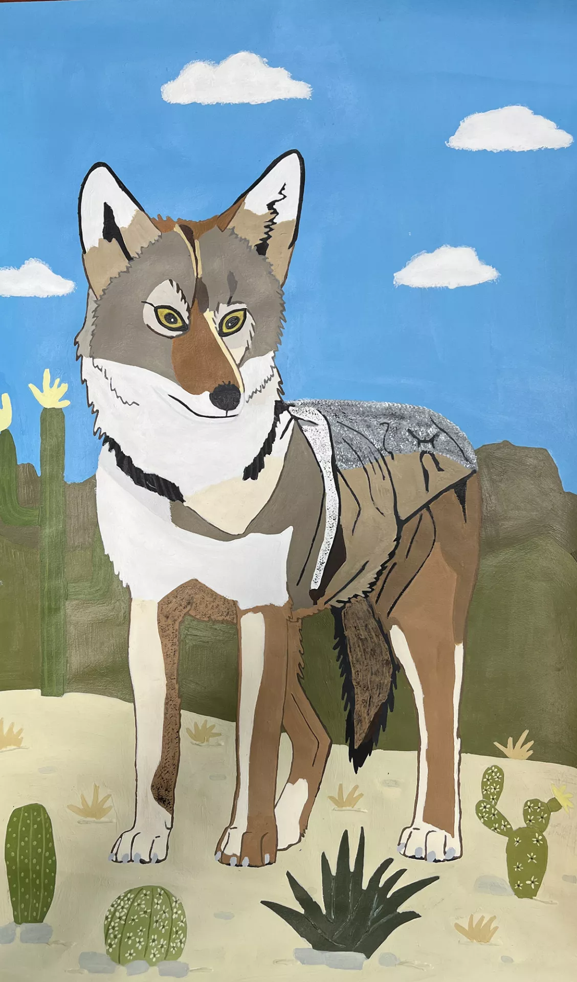 Ariana Sanchez Coyote, 2022 In this painting a coyote stands in a desert environment. The coyote is painted in browns and grays with crisp patches of various tones and textures. There are cacti around and behind the animal. The coyote faces us, its expression calm, its eyes pronounced. In the background is a blue cloudy sky.  Acrylic on paper, 18” x 12”